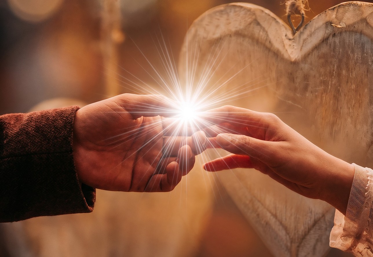 Two hands reaching to touch with radiant light between them and a cross in the background